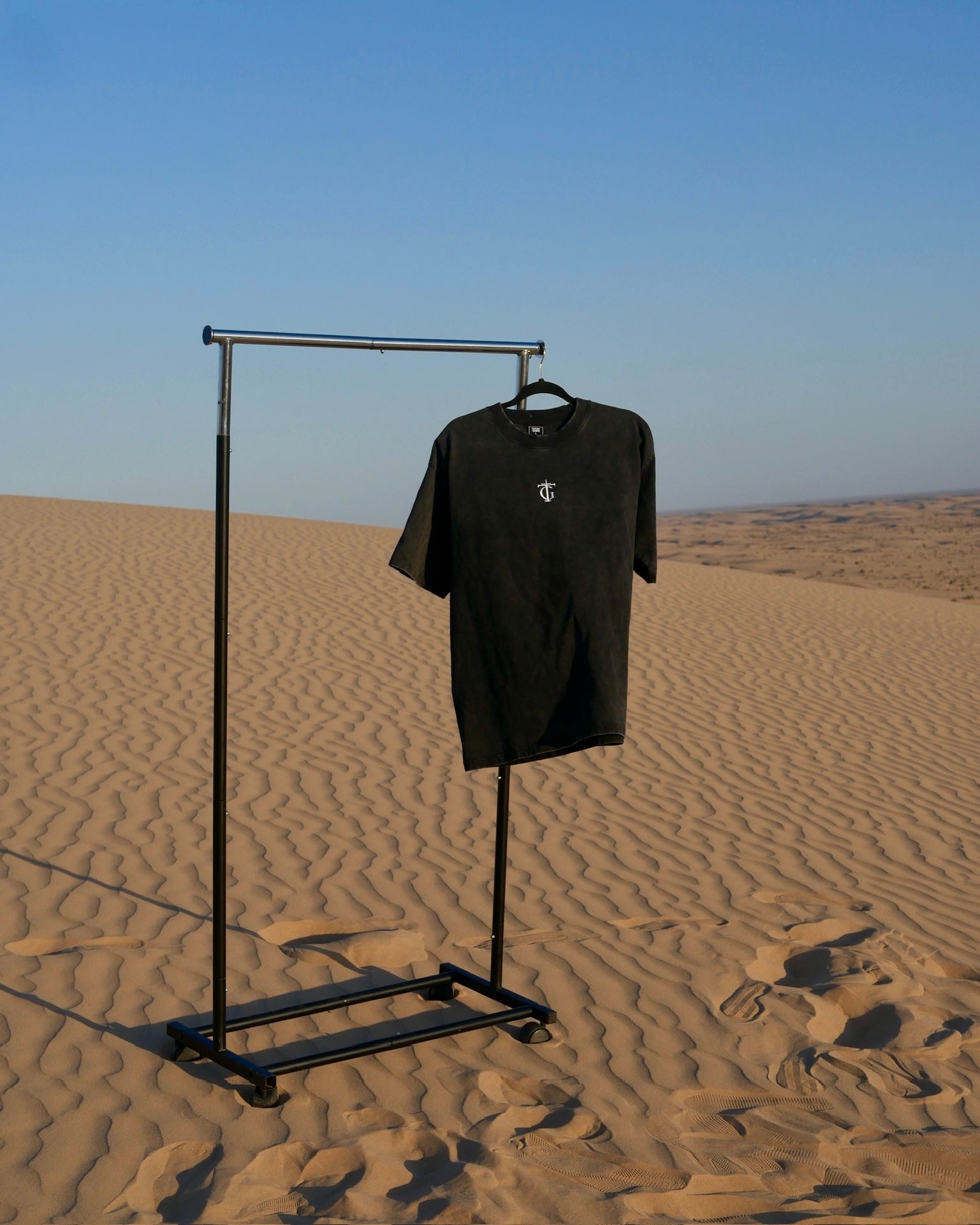 Thank God black sanded Christian tee with TG cross logo hanging on clothing rack in the desert – premium faith-based streetwear showcased in minimalist outdoor setting