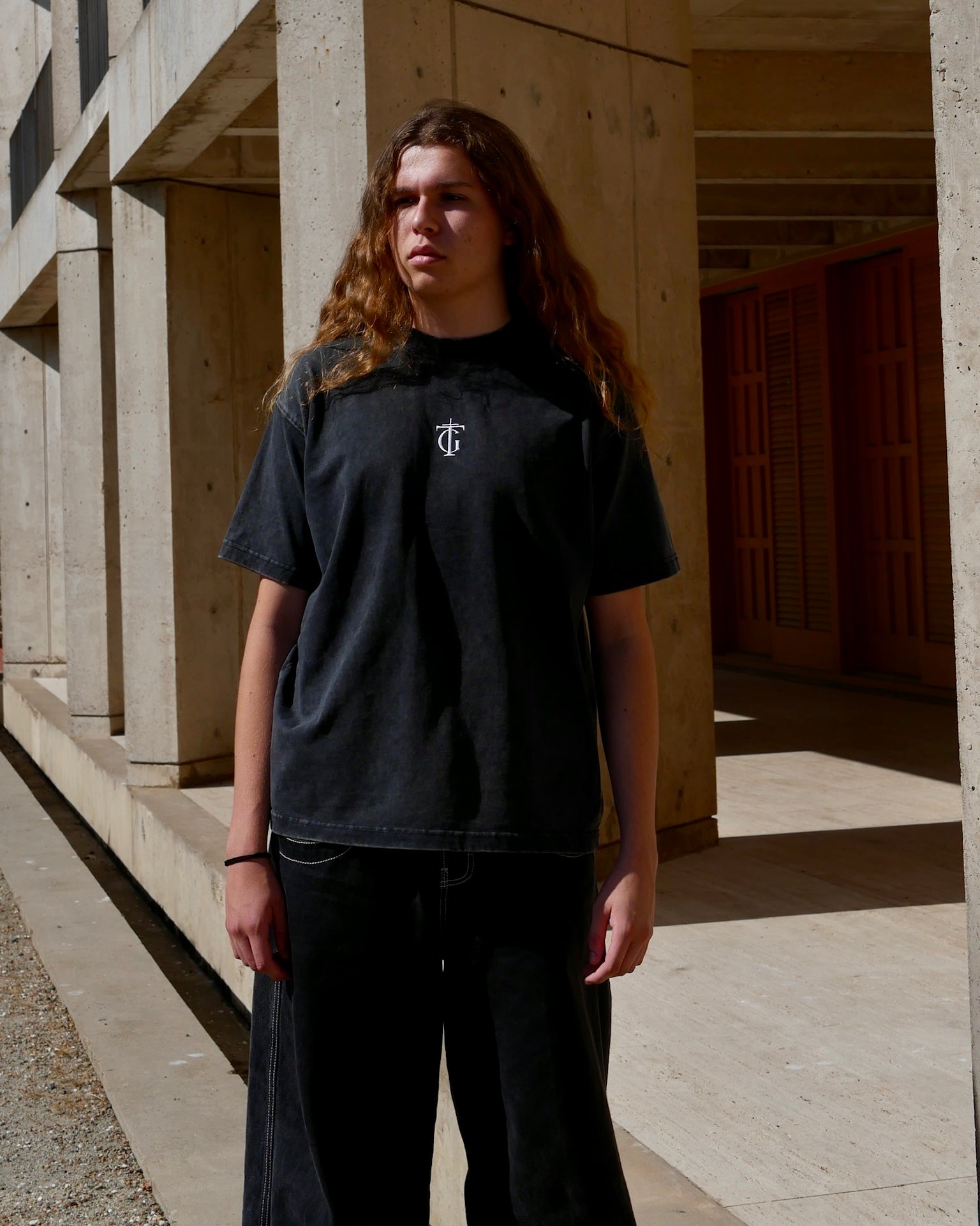 Model wearing black sanded Thank God T-shirt with TG cross logo, standing in cool landscape – Christian streetwear tee made from heavyweight washed cotton, blending faith and fashion.